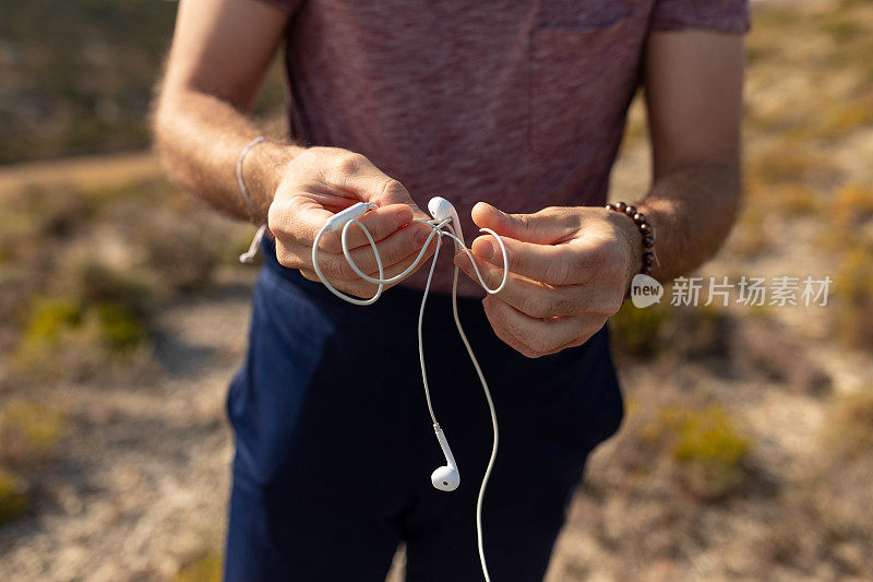 一名男子在乡间散步时，解开一副白色耳机的缆线听音乐
