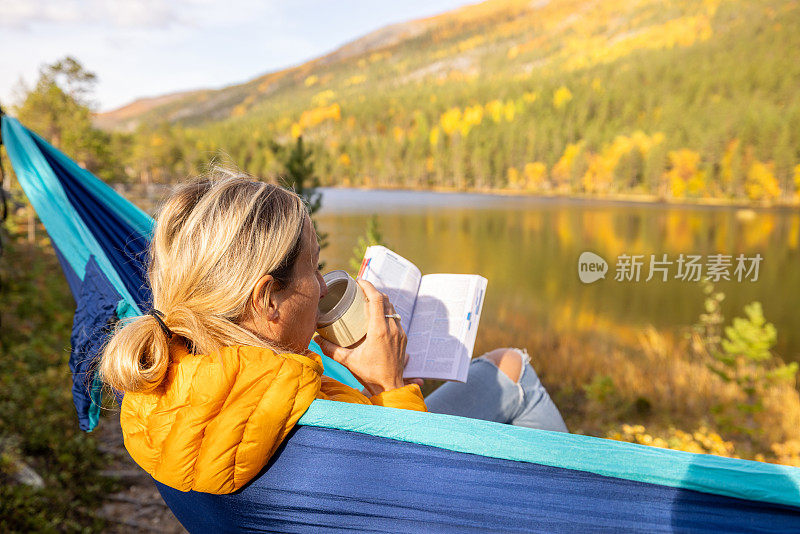 一个女人躺在湖边的吊床上，看书，喝茶，露营