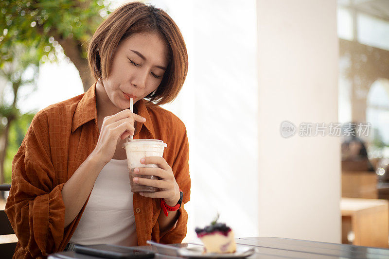 穿着黄衬衫的快乐女士坐在桌边喝着冰巧克力饮料。