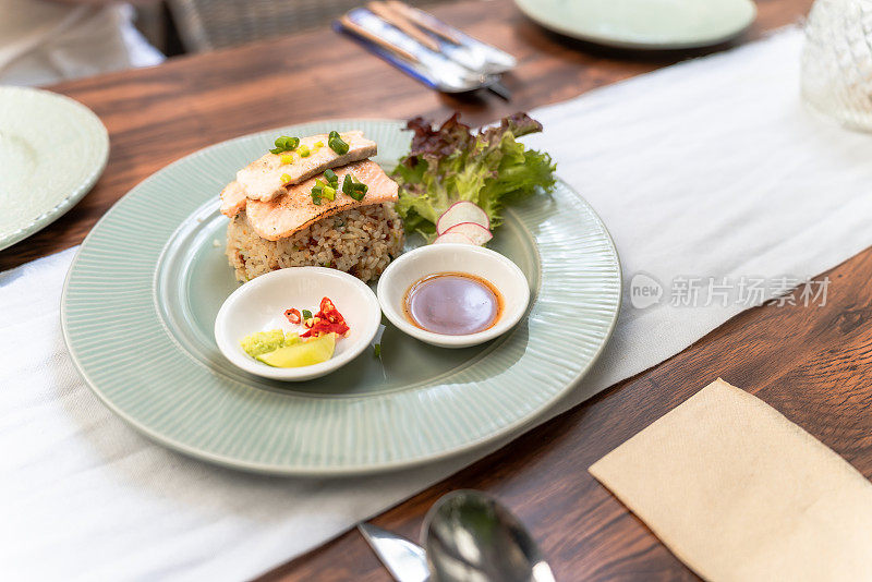 白盘子里的鲑鱼炒饭。美味的三文鱼排和照烧酱饭。泰式辣味糙米炒鲑鱼特写。配菜配蔬菜，柠檬配红辣椒。泰国菜。