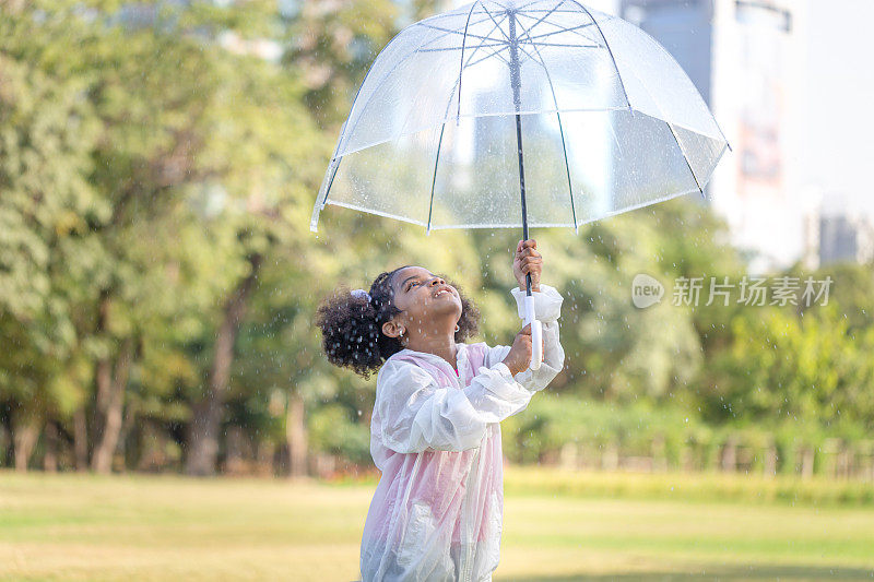 开朗的小女孩撑着伞在公园里打雨，可爱的小女孩在户外的花园里玩耍