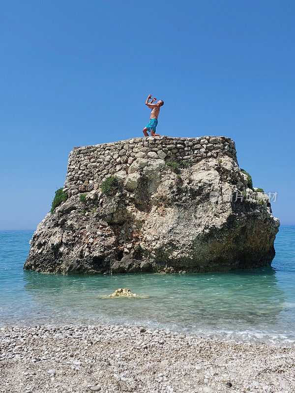 一个快乐的人在美丽的海岸附近的一块大岩石上玩海