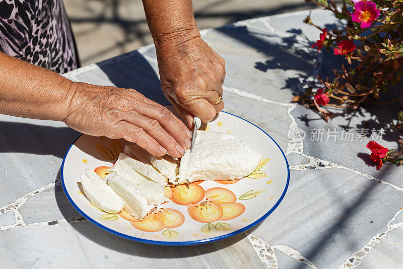 Halloumi，传统的塞浦路斯奶酪。村妇在盘子里切奶酪。