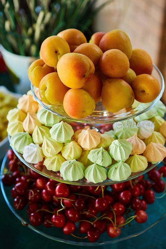 一个三层楼高的盘子，里面有水果和糖果。杏子，樱桃和松软的蛋白派