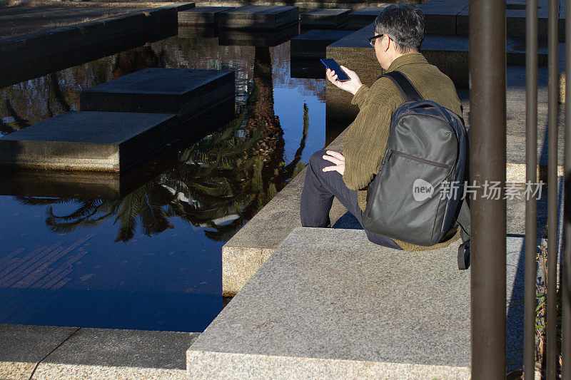 一名男子在户外看手机屏幕的后视图