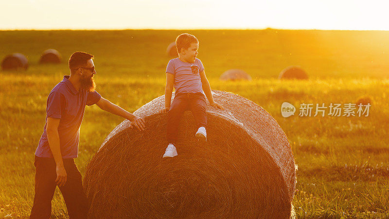 在金色黄昏的薄雾中，一位父亲和他的儿子坐在一个大干草捆上