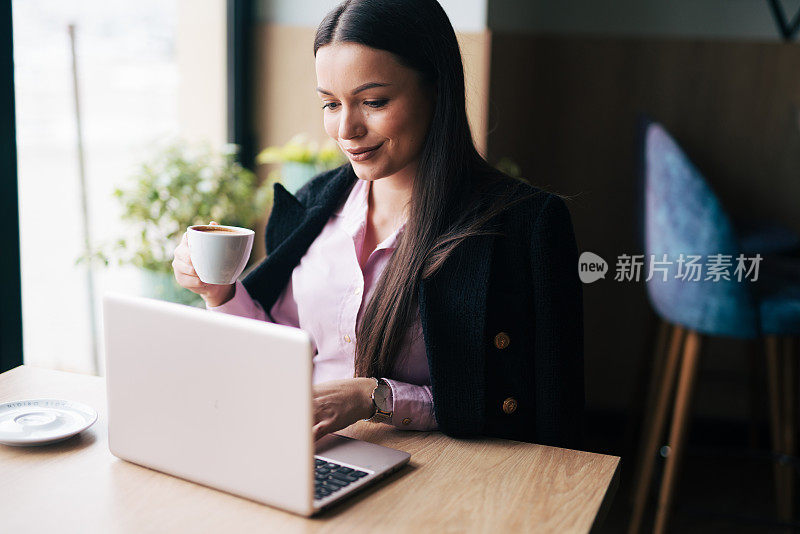 一个漂亮的年轻女人拿着笔记本电脑和一杯咖啡坐在咖啡馆里