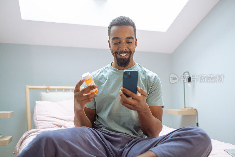 年轻的非裔美国人在卧室里拿着智能手机和药瓶