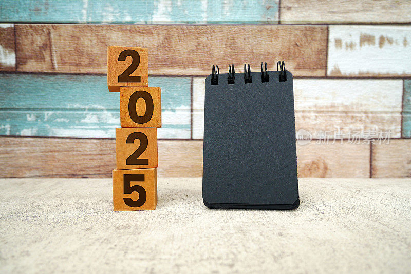刻有2025年的木块和螺旋记事本。2025年新年快乐。