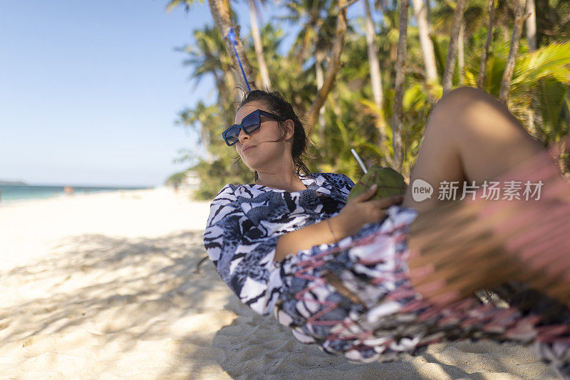 一个穿着夏装的女人躺在吊床上喝着柚子鸡尾酒