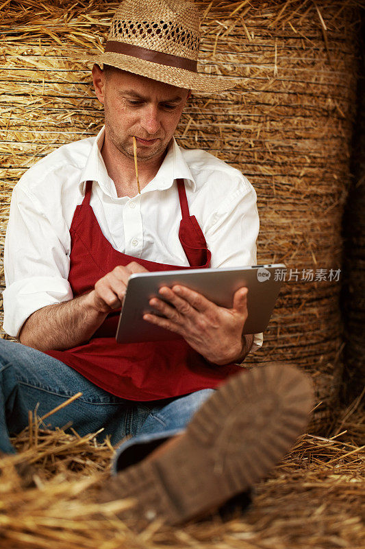 年轻的农民在干草仓里浏览他的平板电脑