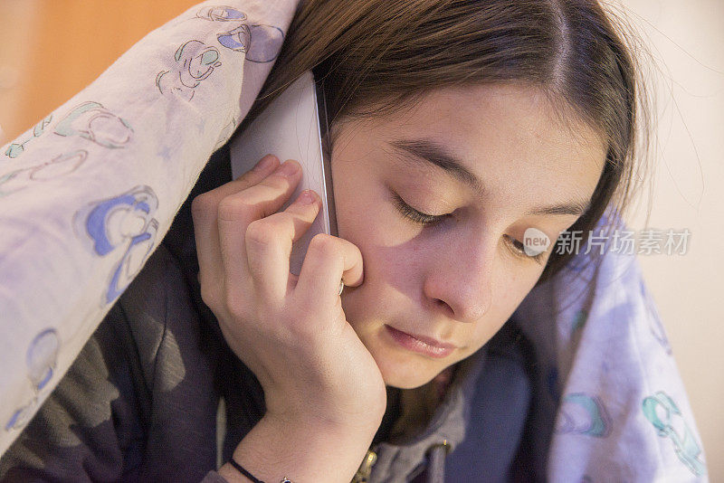 女孩在床上用手机，而躺在毯子下