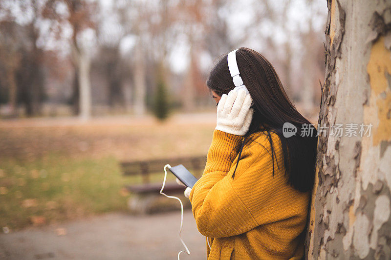 一个女人在当地的公园里戴着耳机听音乐