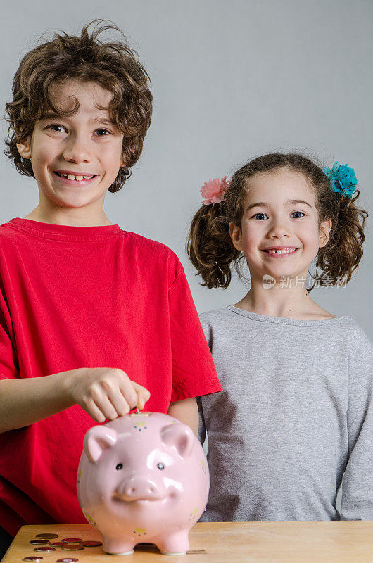 年轻的女孩和男孩微笑着把硬币放入粉红色的储蓄罐
