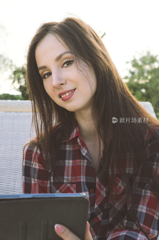 年轻漂亮的女人在公园里享受阳光，用平板电脑