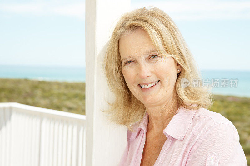 快乐的女人站在她海滨别墅的门廊上