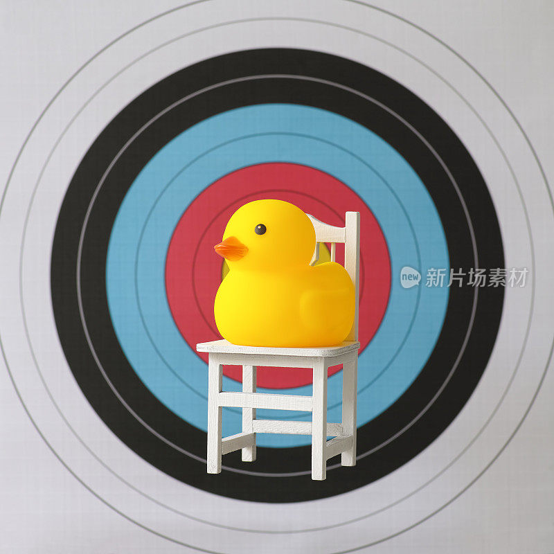 坐在椅子上的黄色橡皮鸭坐在一个体育目标的靶心前。
