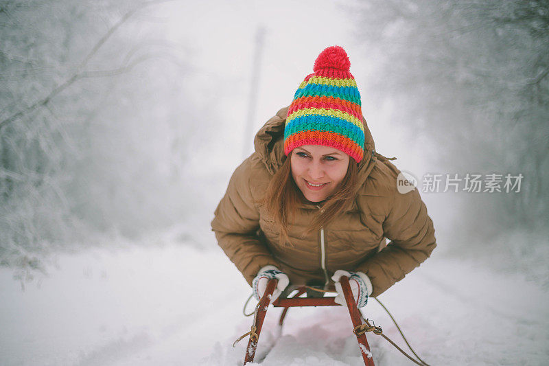 快乐的年轻女子在一个快速的雪橇骑下冰冷的斜坡