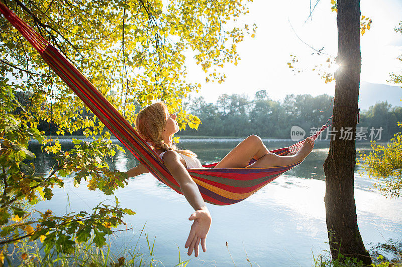 日落时分，女子在河边的吊床上休息。