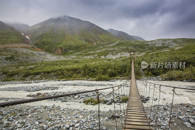 木制悬索桥横跨一条流淌的河流在阿尔