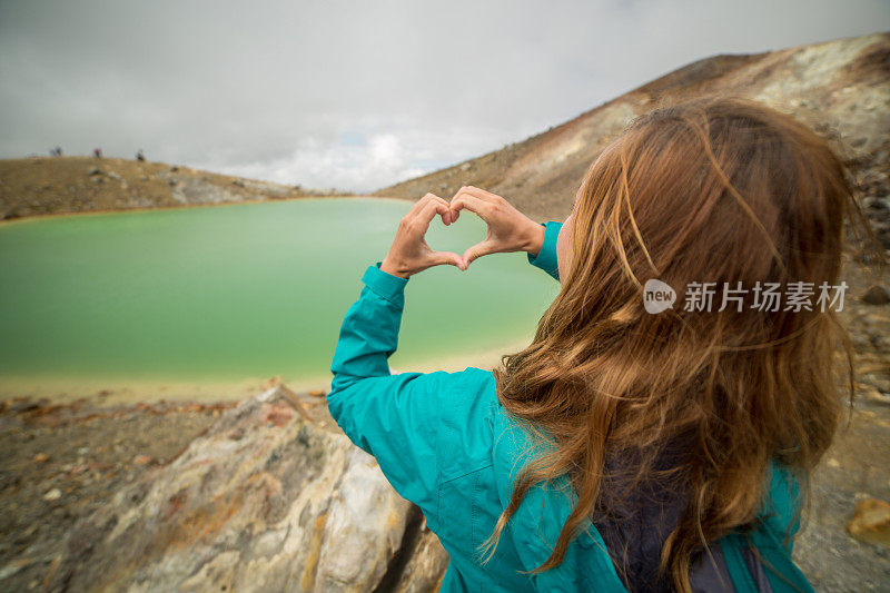 年轻女子朝着山湖做心形手指架