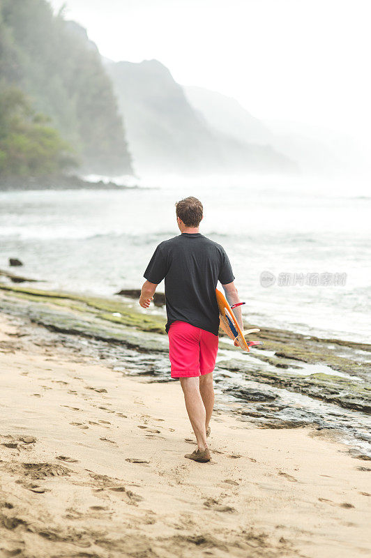 一名25岁左右的年轻人在夏威夷海滩上扛着冲浪板