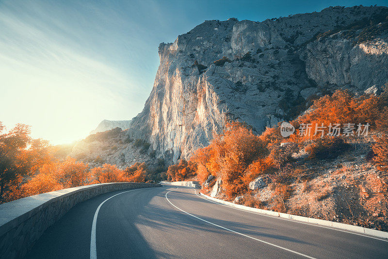 秋天日出时的柏油路。风景优美，空旷的山路上有完美的沥青，高高的岩石，树木和阳光灿烂的天空。古董塑身。旅游的背景。在山区高速公路。自然