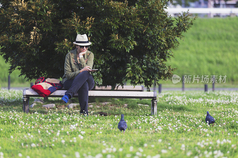 白种妇女在公园长椅上休息，旁边还有鸽子。
