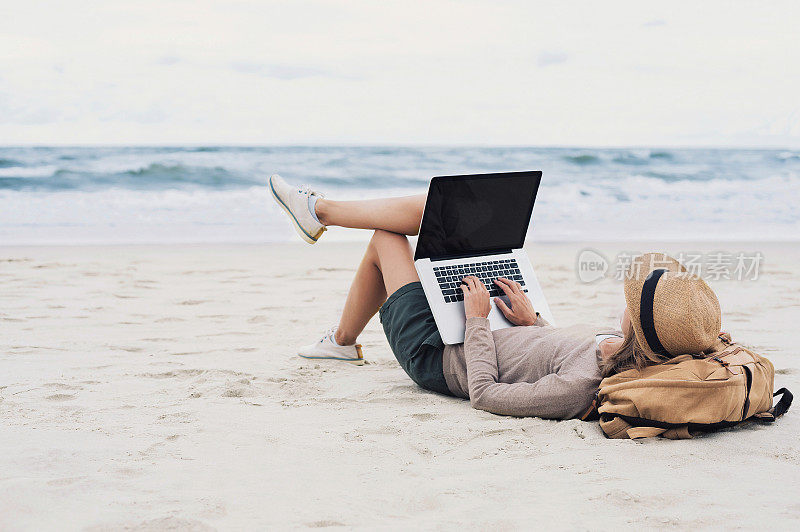 年轻女子在海滩上用笔记本电脑