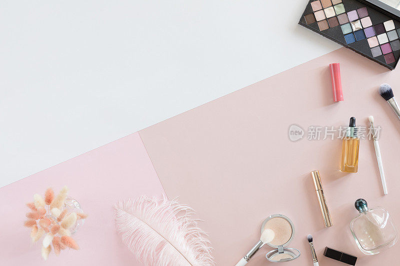 俯视图的一套妇女装饰化妆品在粉彩背景，平lay。女性的工作空间配有美容饰品和鲜花