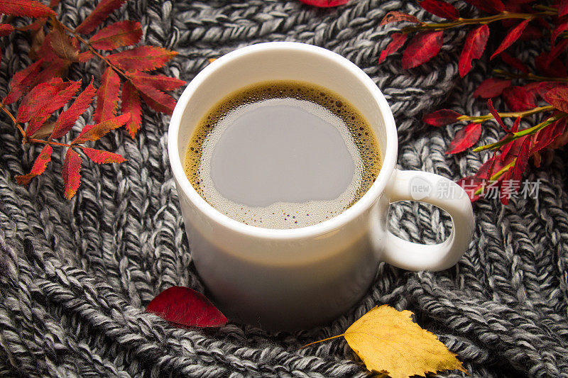 木桌上放着一杯秋天的热咖啡，还有针织围巾和毛衣。舒适、温馨、舒适。