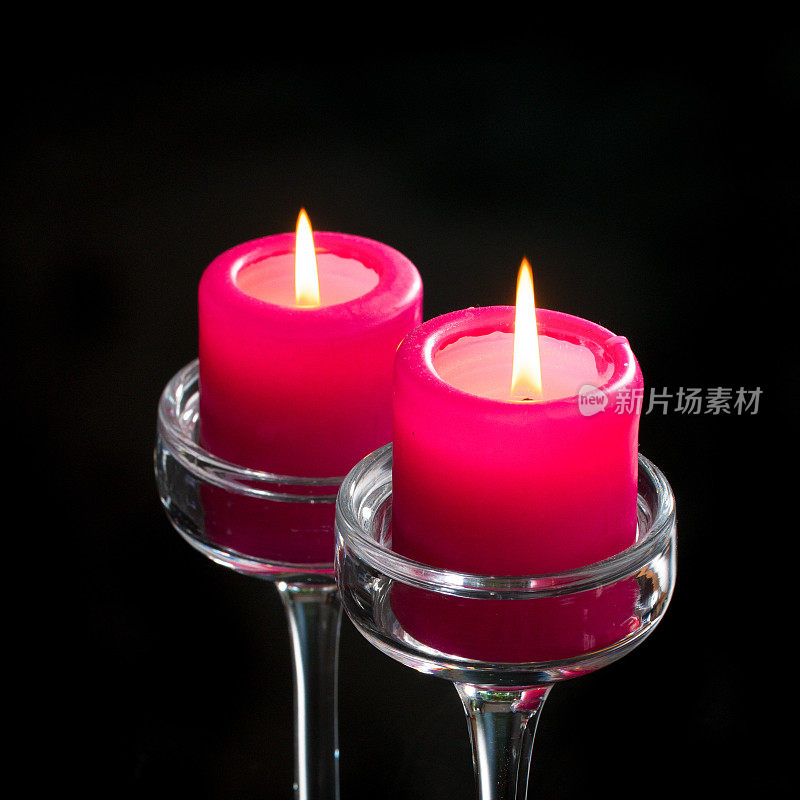 玻璃烛台上的两支红色蜡烛在黑色的背景下燃烧着