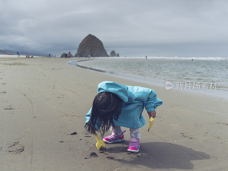 亚洲小女孩在沙滩上玩玩具铲子