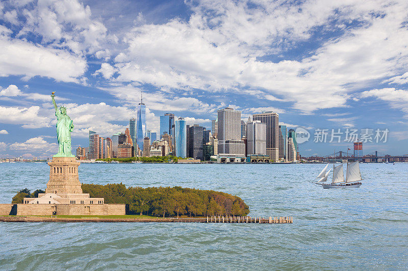 自由女神像和纽约城市天际线，曼哈顿金融区，世界贸易中心，帆船(高船)，纽约港水，炮台公园，布鲁克林桥，曼哈顿桥和蓝天。