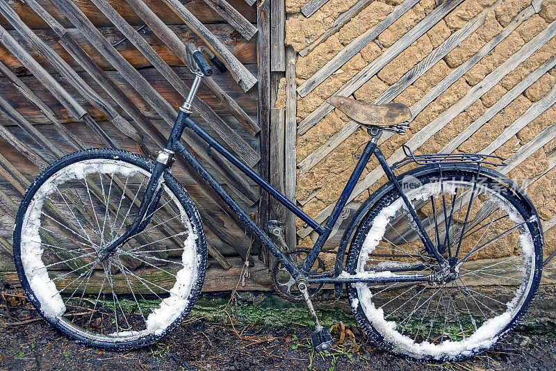 旧自行车在雪地里靠近棕色的墙