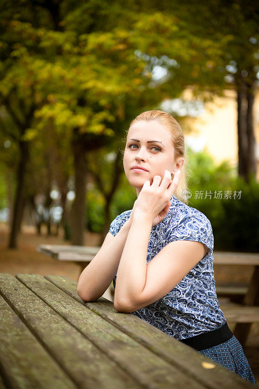 女孩坐在秋天的公园里望着远方。