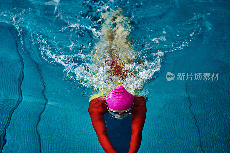 身着红色套装、戴着眼镜的女游泳运动员为了掉头而沉入水中。水花四溅向不同的方向。