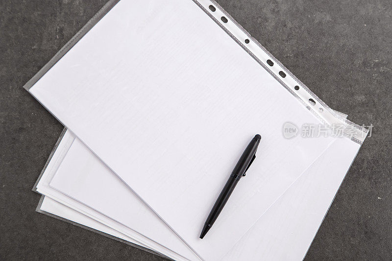 一只黑色的笔在一张白纸上，在一张灰色的桌子上。从上往下看
