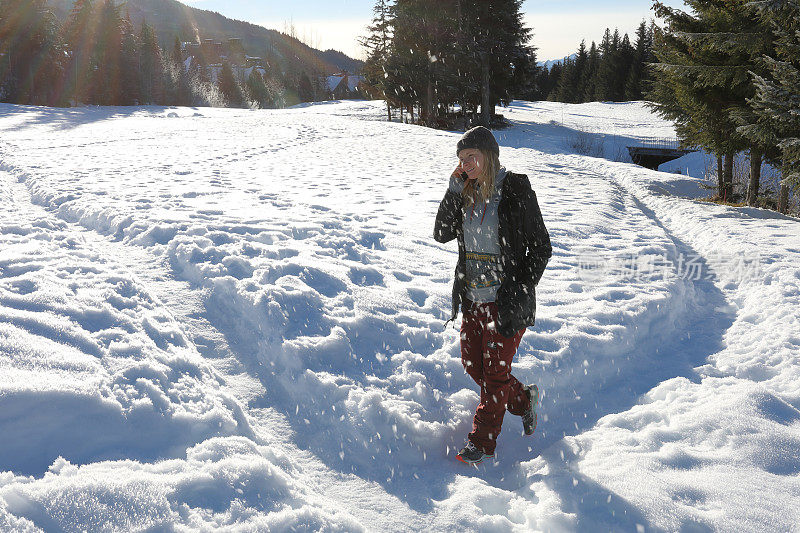 一个年轻女子一边打电话一边走在雪道上