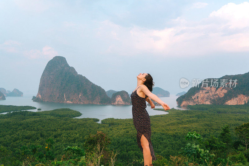 一名女子高举手臂站在攀牙湾的背景上