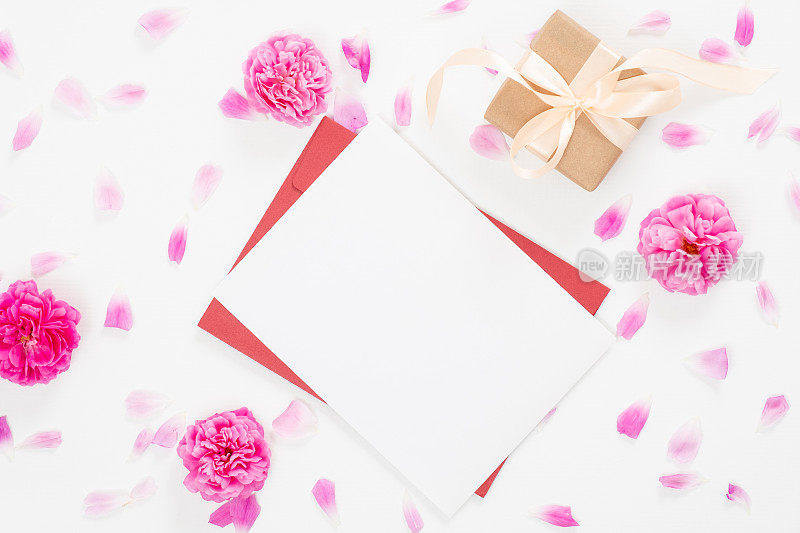 俯视图空白纸卡，红包，礼盒，玫瑰花蕾和花瓣在白色的背景。简约平铺风格构成，情书、贺卡概念。