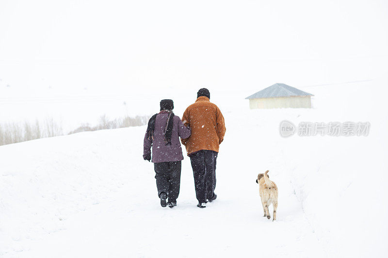 一对老年夫妇在下雪的乡村路上穿着暖和的衣服