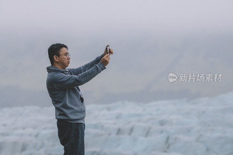 一名亚洲中国游客在阴天里用手机拍摄冰岛冰川的照片