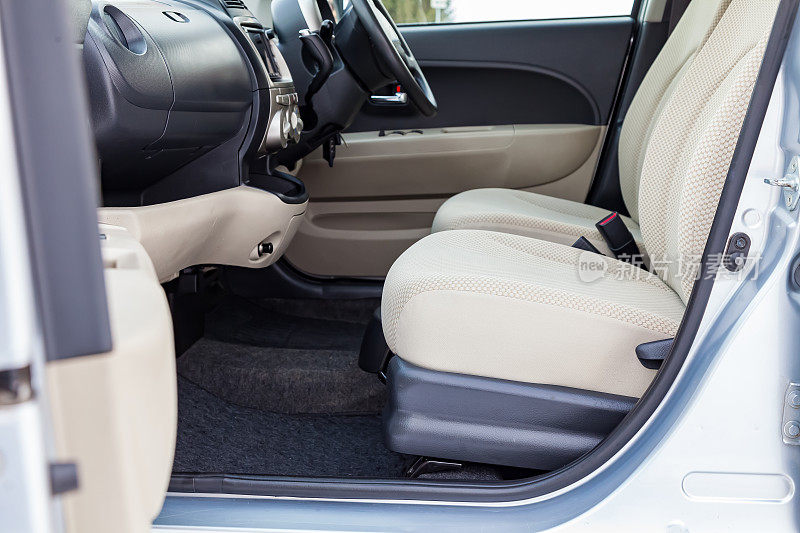舒适的前排座位内的汽车:司机和乘客，与米色velourus，现代室内设计，方向盘覆盖和豪华的中控台。