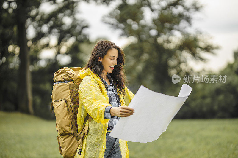 年轻女子穿着防水夹克，看地图，在雨中徒步旅行