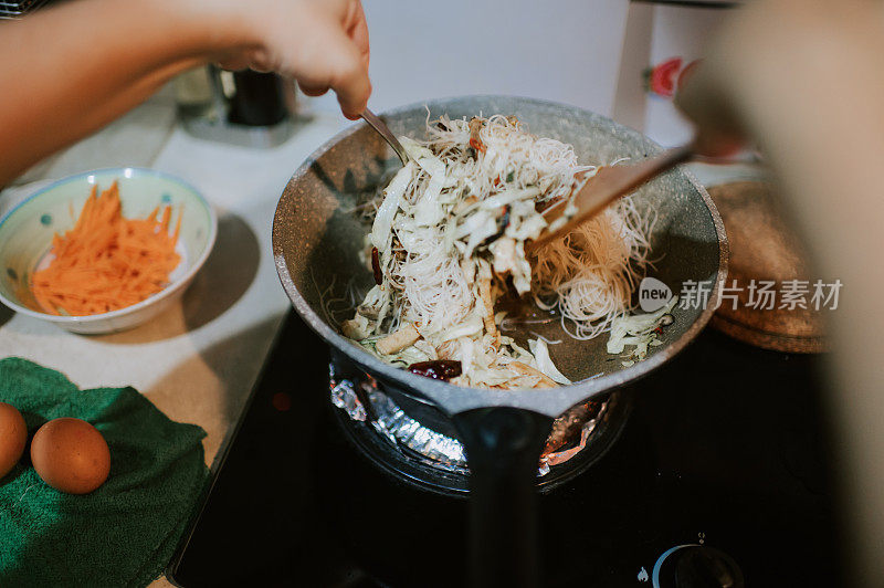 一名亚洲华人女子在厨房里用平底锅和炉子煮炒面