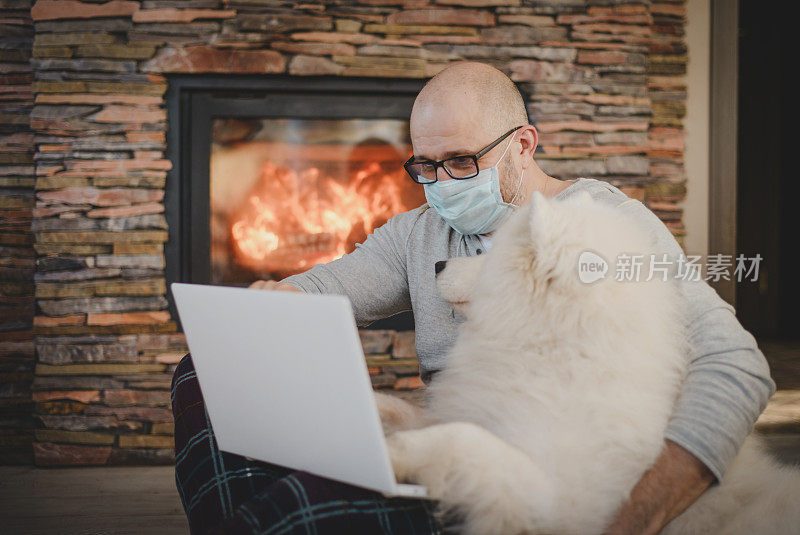 成年男子戴着面具在家工作，使用笔记本电脑(狗，壁炉)