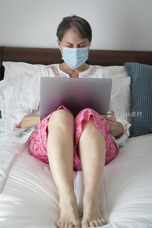 妇女生病在床上戴口罩使用笔记本电脑