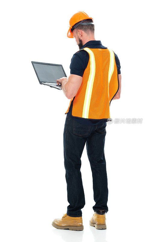 建筑工人站着，穿着衬衫，拿着锤子，使用笔记本电脑