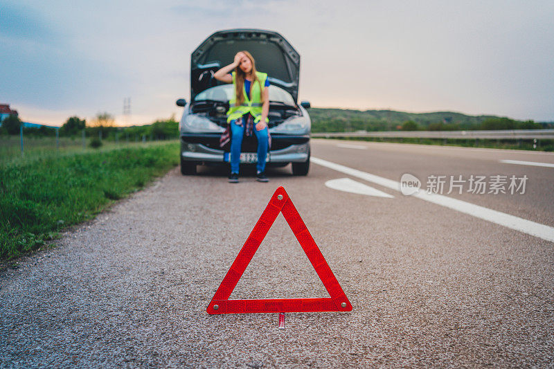 女人在一辆车抛锚后用三角形警告